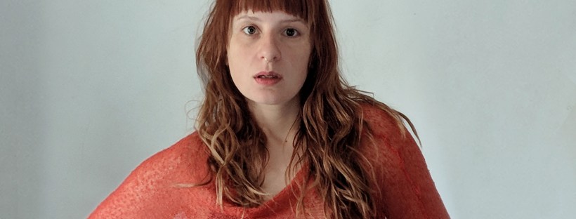 young woman standing, giving direct eye contact draped in fiery orange shawl as if standing in flame.